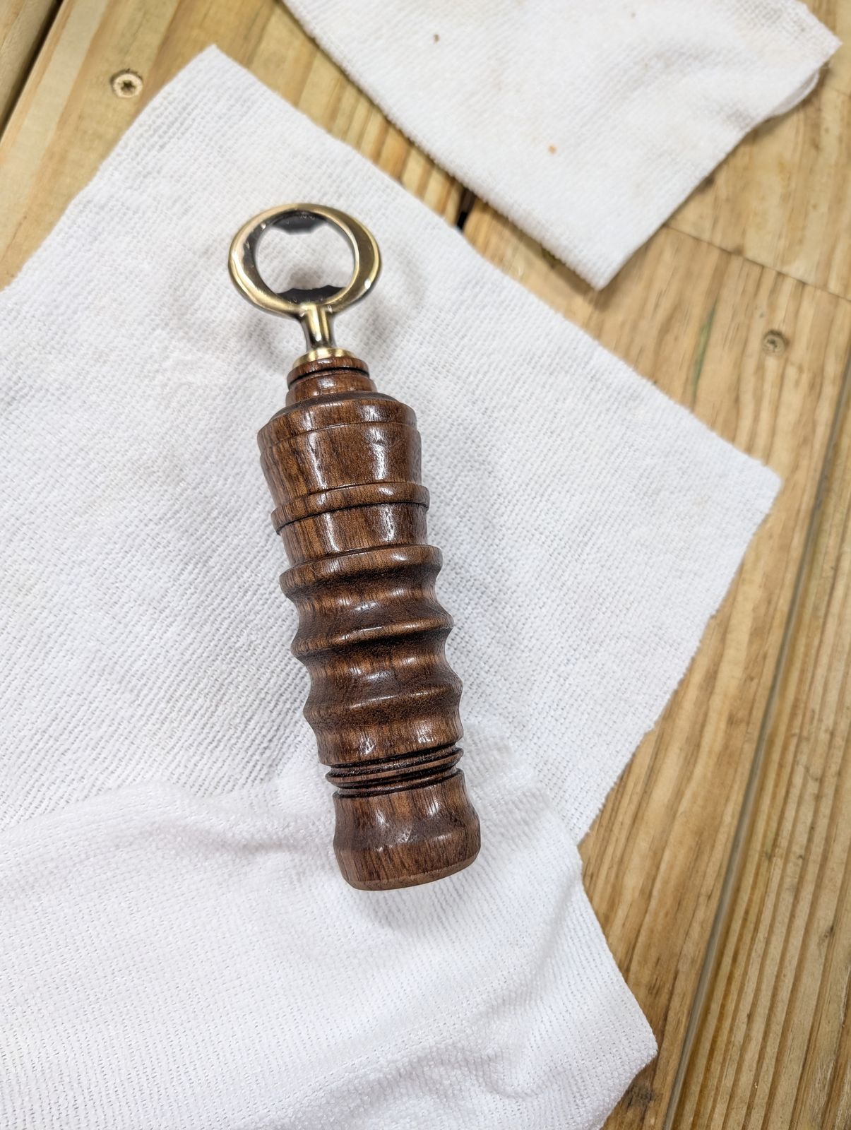 A hand-turned walnut bottle opener standing on a towel on the workbench